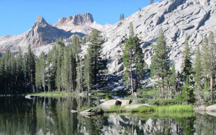 An alpine lake rests among evergreen trees and gray mountains 